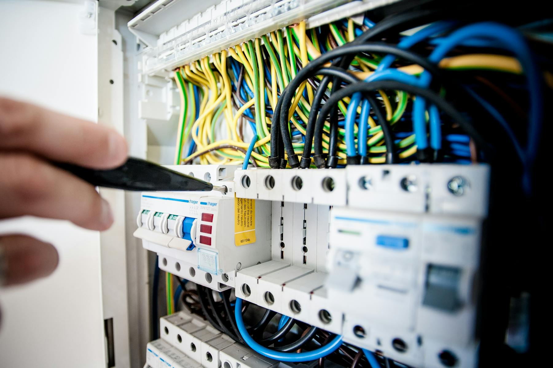 A CookTech field tech working inside an open electrical switchboard with a drill